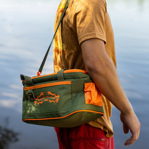 Thumbnail of Man with a green and orange bag by a lake