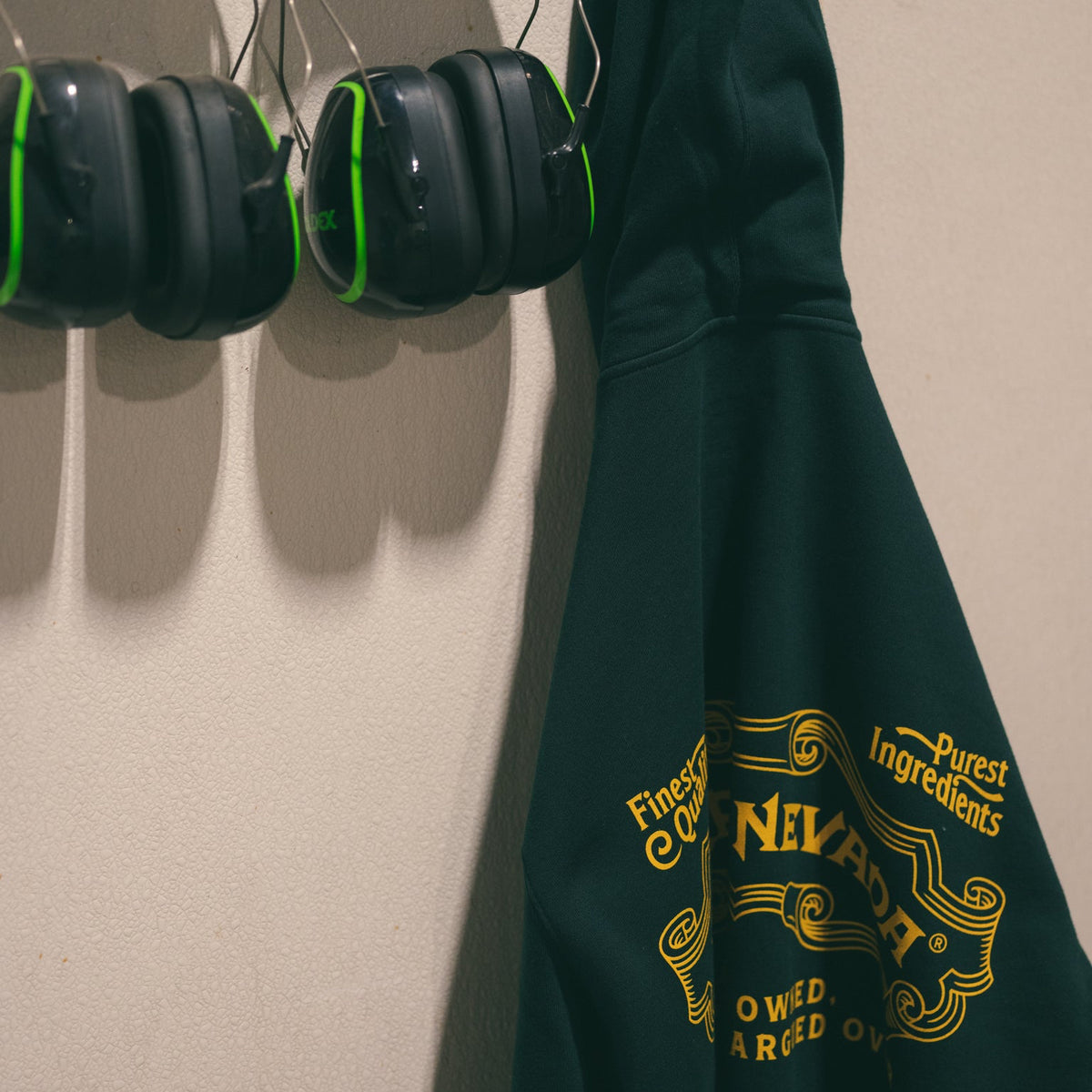 Green hoodie with yellow text hanging on a hook next to black ear protection.