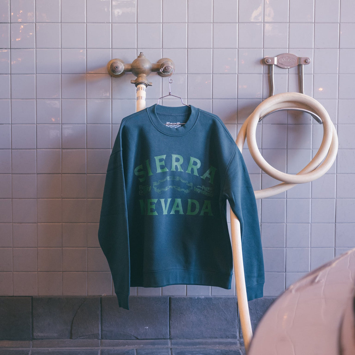 Green sweatshirt with 'Sierra Nevada' text hanging on a rack against a tiled wall.
