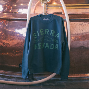 Thumbnail of Green sweatshirt with 'Sierra Nevada' text hanging on a copper pipe against a textured wall.