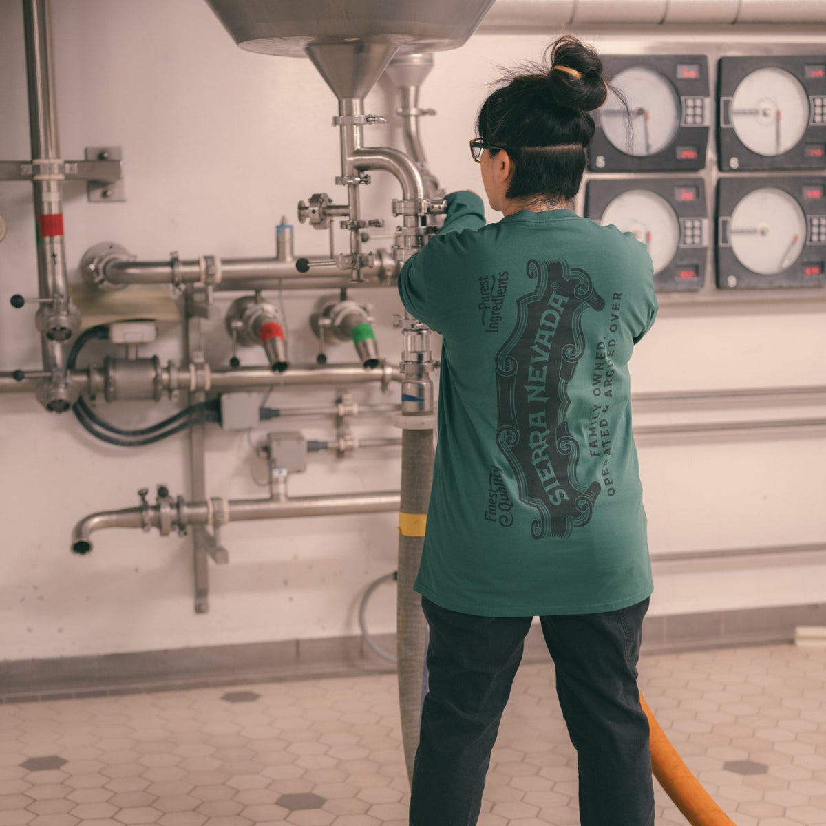 Person in a brewery wearing a green shirt with 'Sierra Nevada' branding, working with equipment.