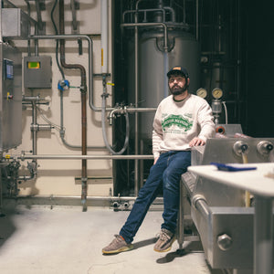 Thumbnail of Person sitting on a metal bench in a industrial setting with machinery and pipes.