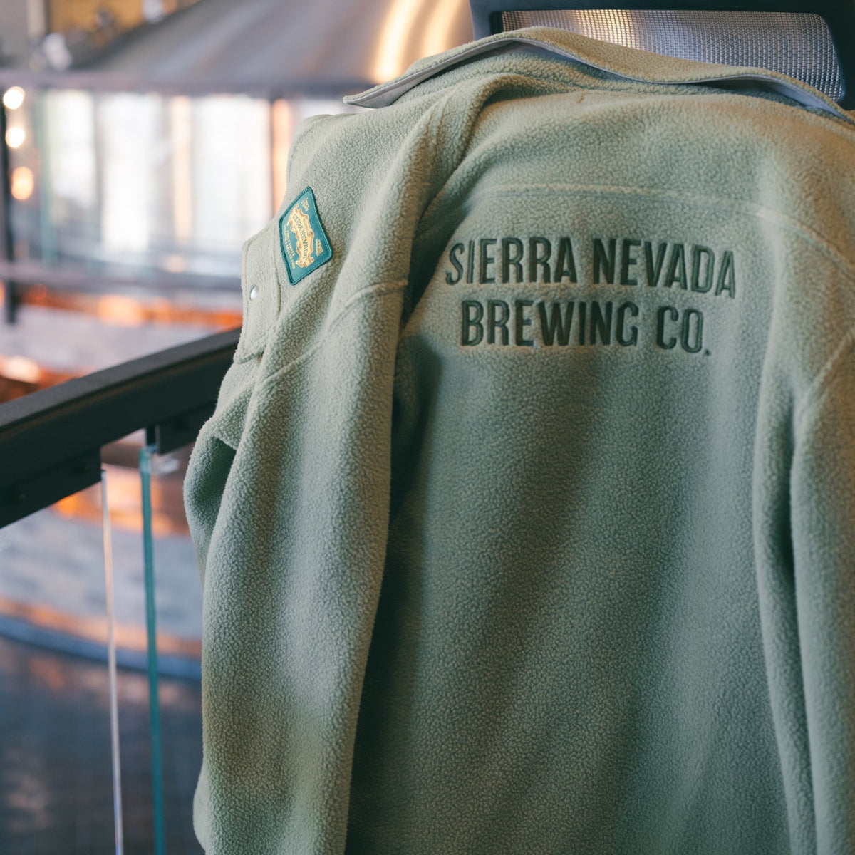 Green jacket with Sierra Nevada Brewing Co. logo on a blurred indoor background