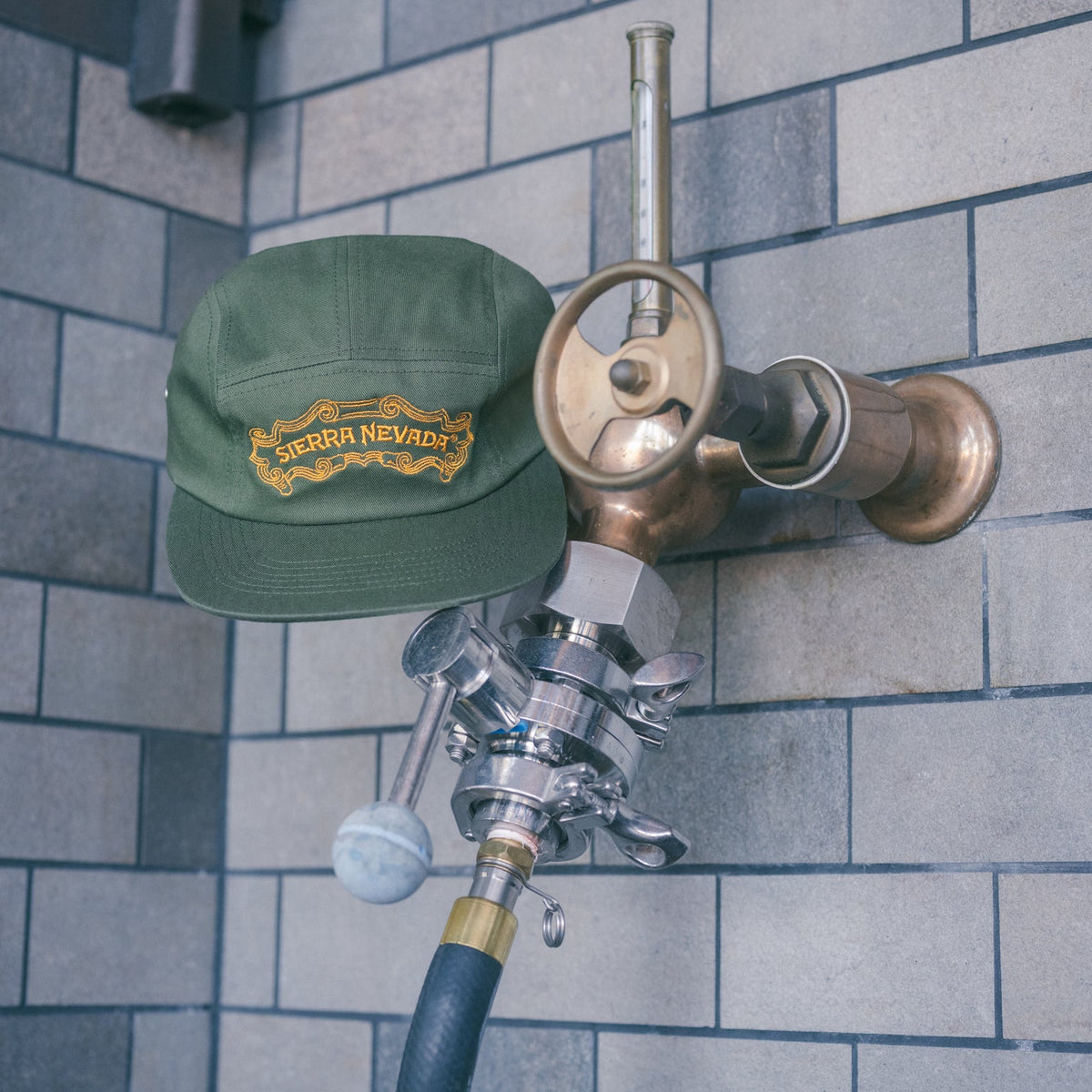 Green cap with a logo on a beer tap against a tiled wall.