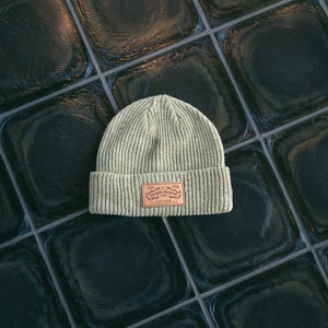 Thumbnail of Green beanie with a leather patch on a reflective tiled surface