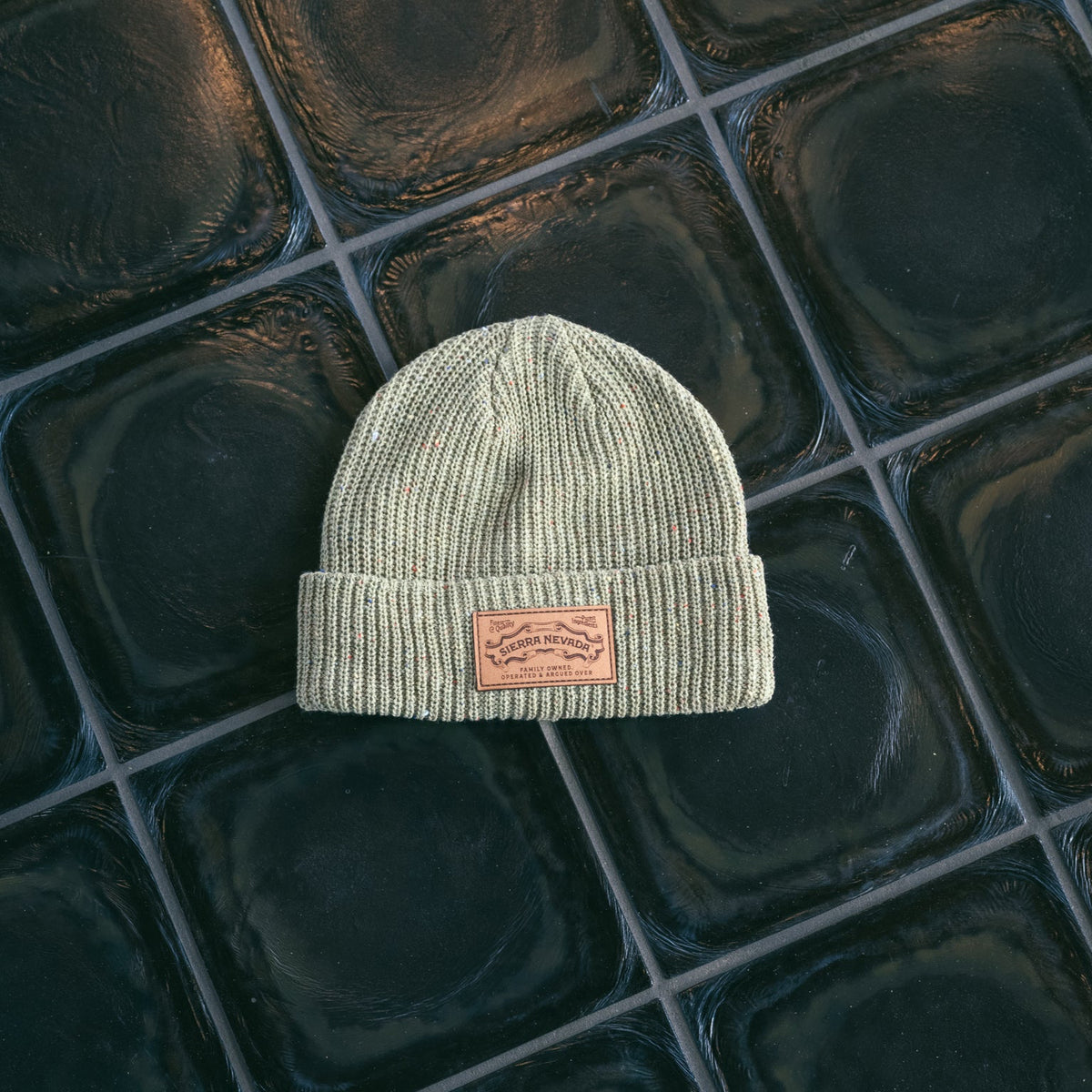 Green beanie with a leather patch on a reflective tiled surface