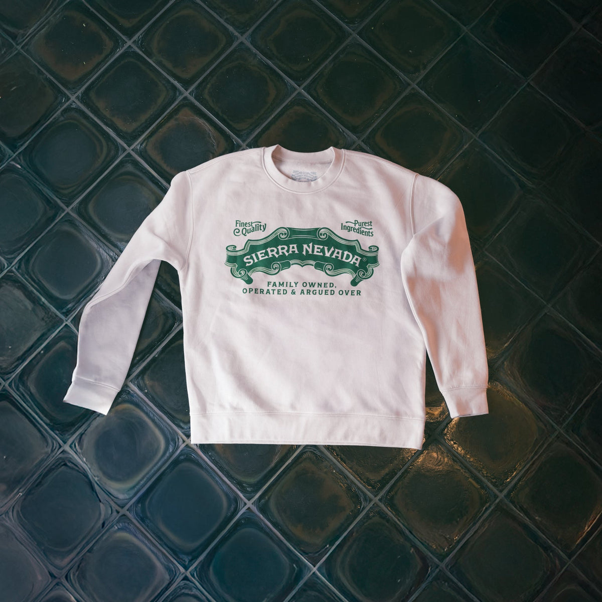 White sweatshirt with green text on a dark tiled floor