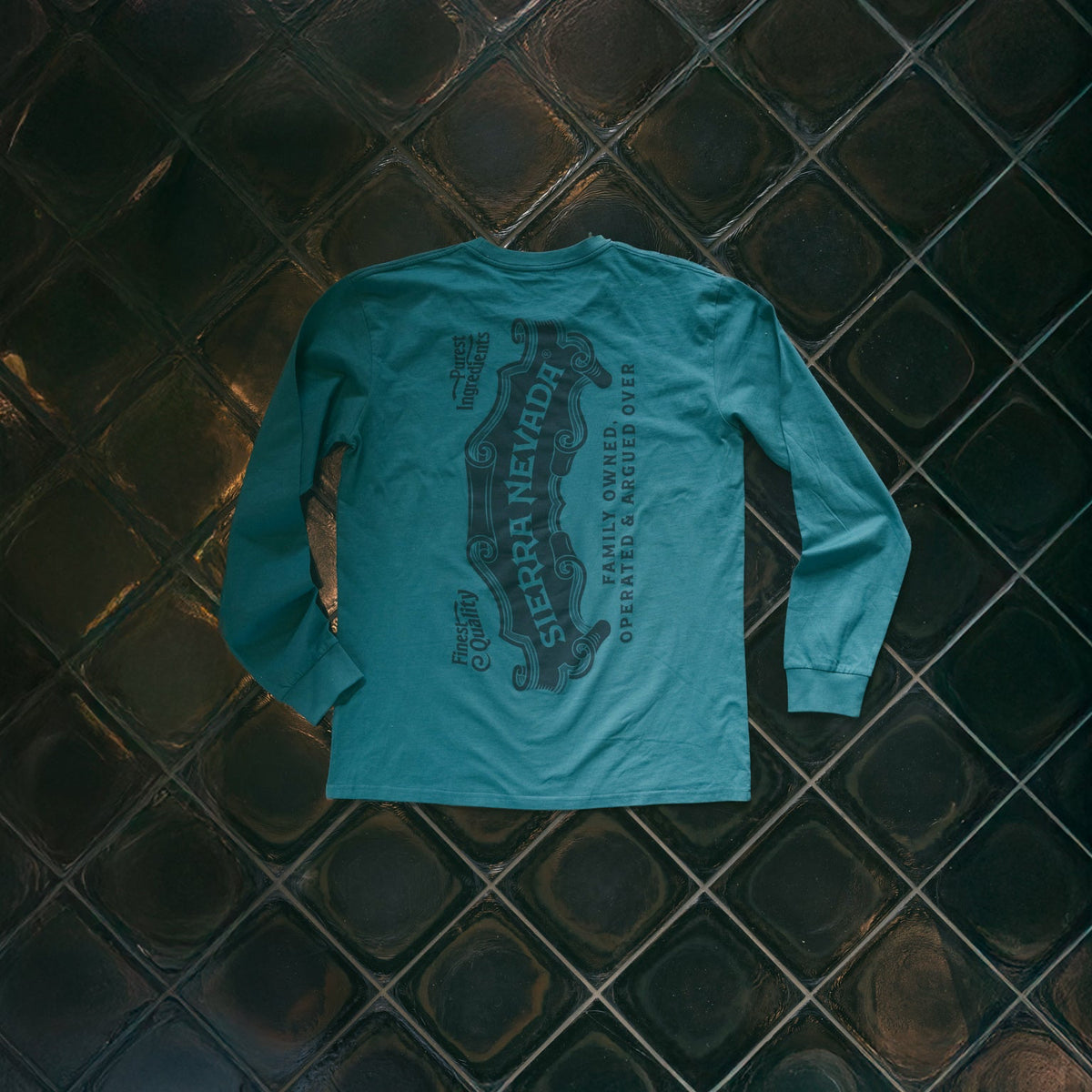 Green long-sleeve shirt with graphic design on a dark tiled floor