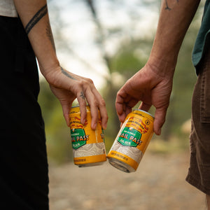 Thumbnail of Sierra Nevada Brewing Co. Trail Pass Golden Non-Alcoholic Brew - Two friends on a hike cheers with two cans of Trail Pass Golden
