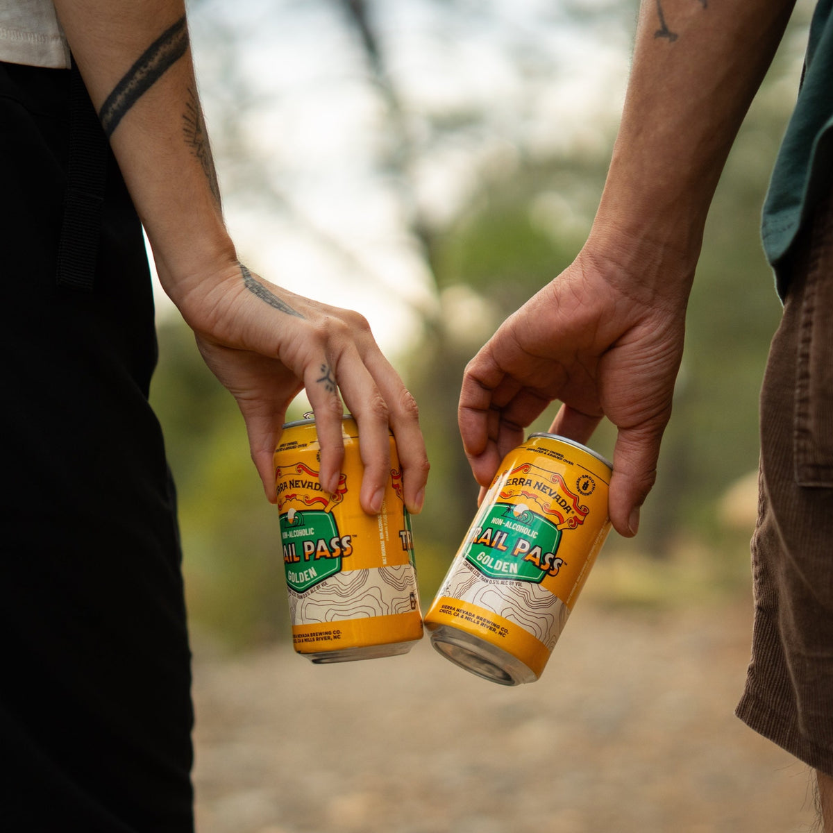 Sierra Nevada Brewing Co. Trail Pass Golden Non-Alcoholic Brew - Two friends on a hike cheers with two cans of Trail Pass Golden