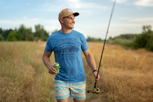 Thumbnail of A man wears the Sierra Nevada Brewing Co. Handcrafted T-Shirt while walking along a riverbank carrying a fishing pole and a Pale Ale.