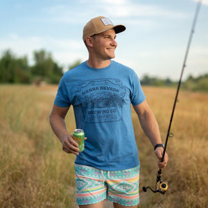 Thumbnail of A man wears the Sierra Nevada Brewing Co. Handcrafted T-Shirt while walking along a riverbank carrying a fishing pole and a Pale Ale.