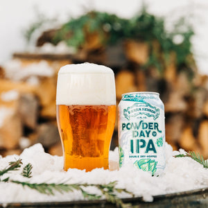 Thumbnail of Sierra Nevada Powder Day IPA poured into a pint glass beside a can on a tabletop covered in snow