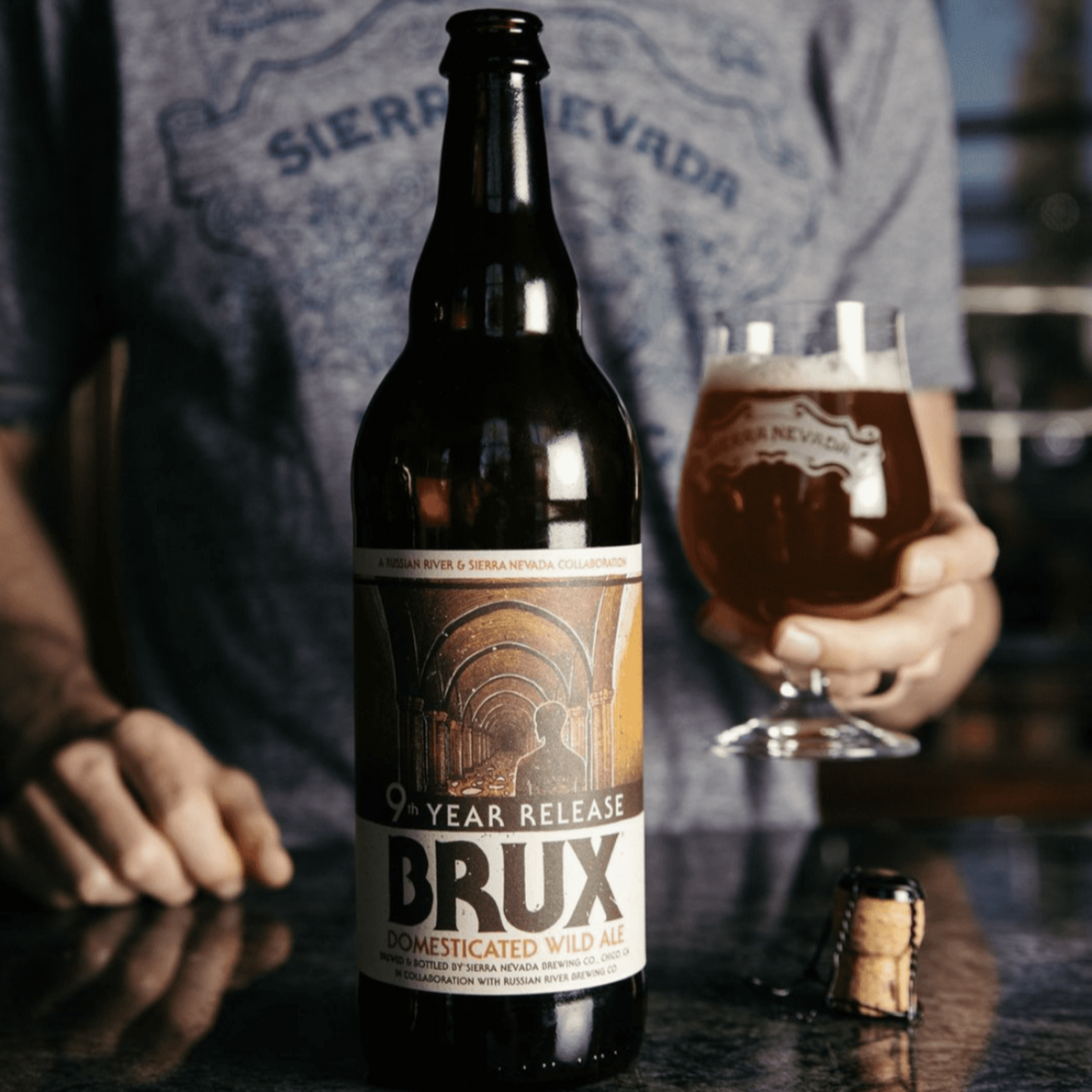 A bottle of Brux sits on a bar in front of a man, alongside a freshly poured pint