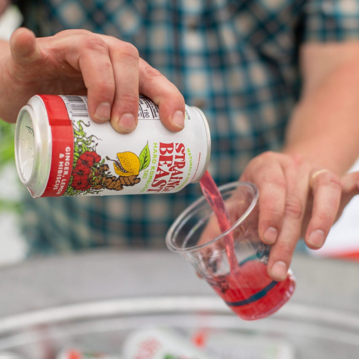 A person pours a can of Strainge Beast Ginger, Lemon and Hibiscus kombucha into a glass