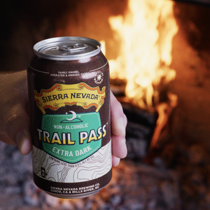 Thumbnail of Hand holding a Sierra Nevada Trail Pass Extra Dark non-alcoholic beer can in front of a fireplace.