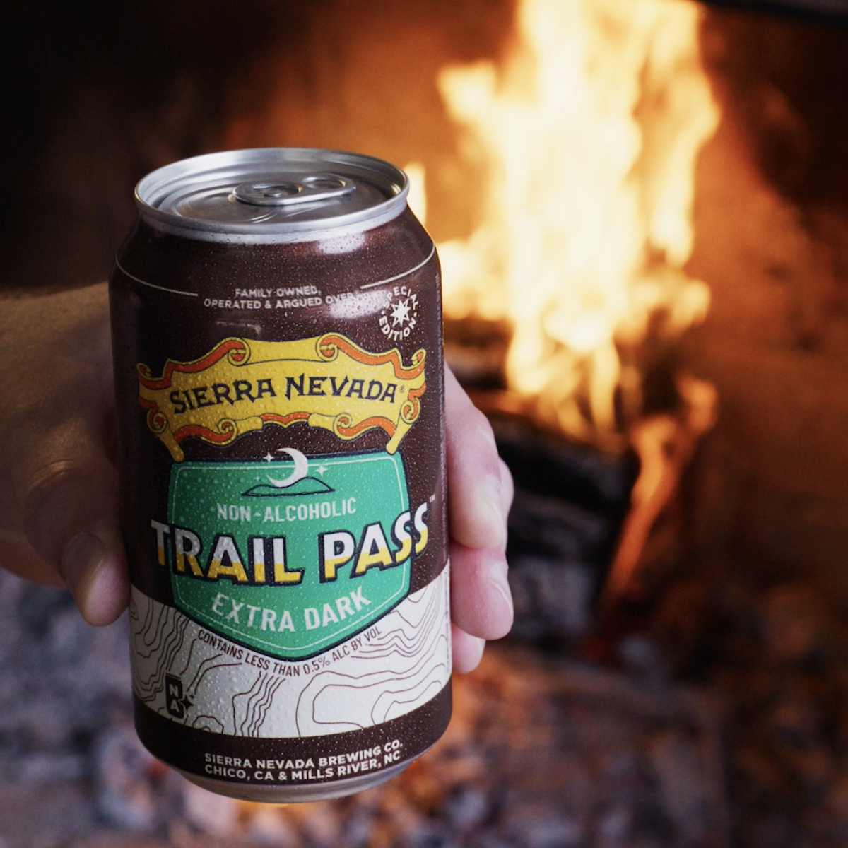 Hand holding a Sierra Nevada Trail Pass Extra Dark non-alcoholic beer can in front of a fireplace.