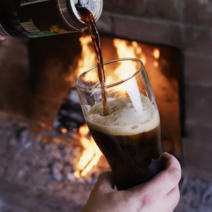 Thumbnail of Pouring dark liquid into a glass with a fireplace in the background