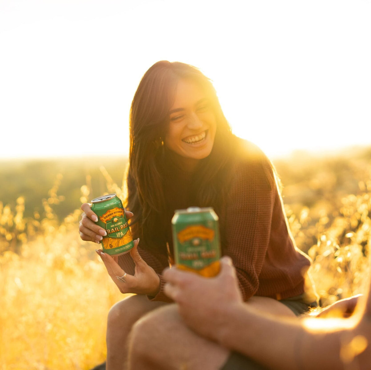 A woman sits beside a man and laughs while holding a can of Sierra Nevada Trail Pass IPA