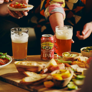 Thumbnail of A can and glass of Sierra Nevada Celebration IPA on a coffee table covered with snack foods