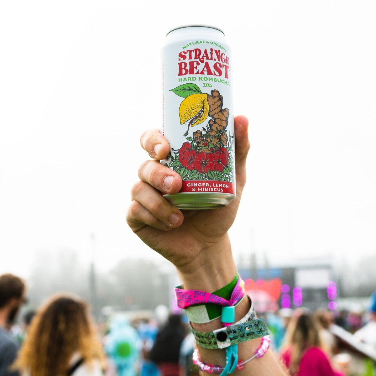 Person in a crowd holding a can of Strainge Beasts Ginger, Lemon & Hibiscus hard kombucha