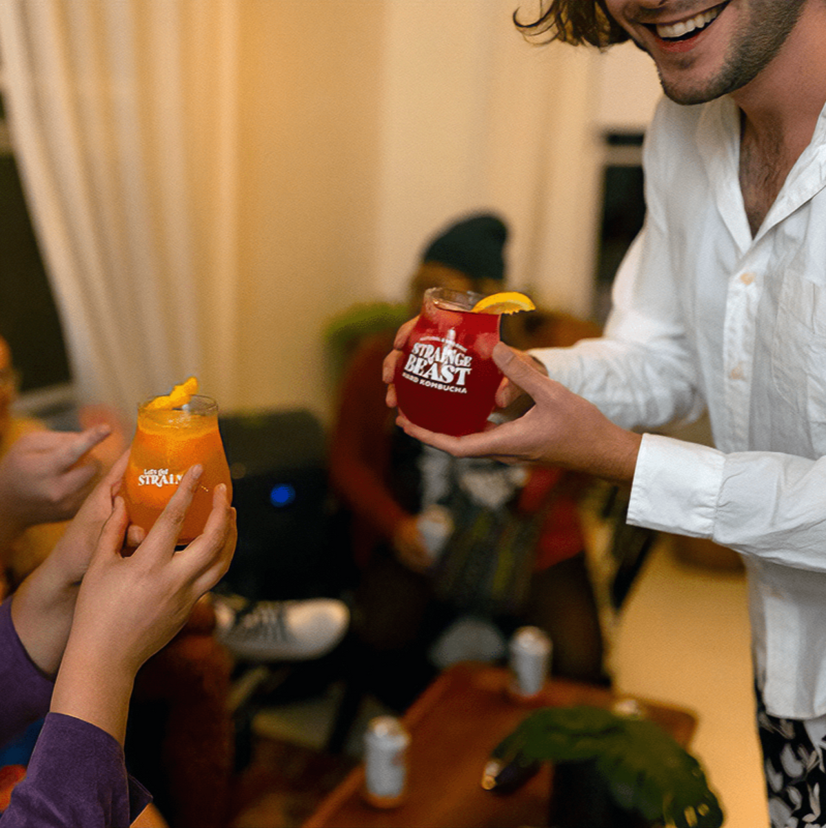 Two friends raising glasses of Strainge Beast hard kombucha and smiling