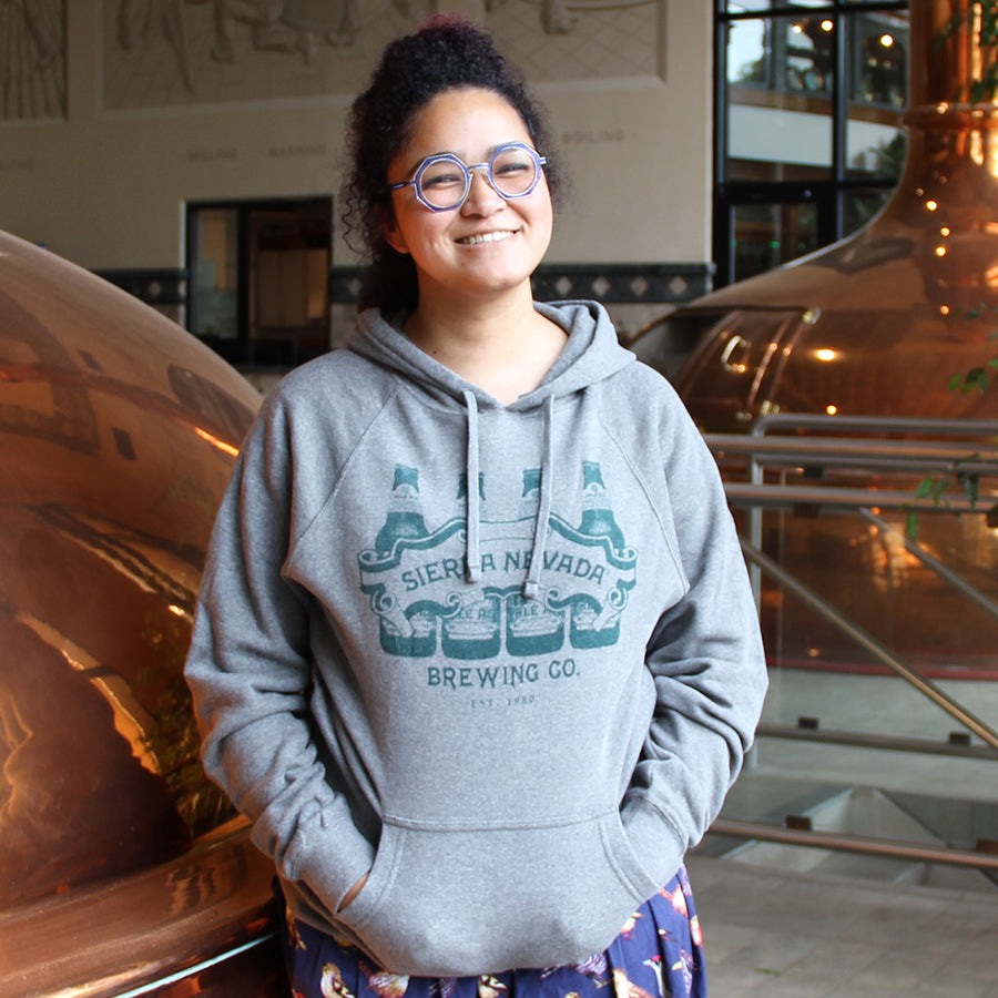 Woman with curly dark hair and glasses wearing the bottle line up hoodie.